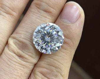 May include: A large, round-cut diamond with many facets, reflecting light in a dazzling display of colour. The colourless gemstone is held in a hand, showcasing its size and clarity. The diamond's cut maximises its sparkle.