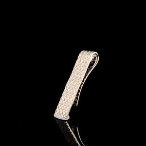 May include: A silver-toned tie clip, encrusted with small, sparkling stones. The clip has a curved top and a rectangular body, reflecting light against a black background. The accessory is designed to secure a tie.