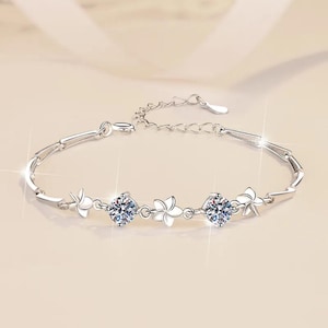 May include: A silver bracelet with a delicate chain and three small flower charms with clear cubic zirconia stones.