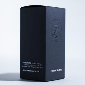 May include: A black perfume oil box with embossed logo and text. The box features the text "INGREDIENTS: alcohol denat., fragrance materials. For an extended list of ingredients see: BLACKSWANSOCIETY.COM PERFUME OIL 30 ML."