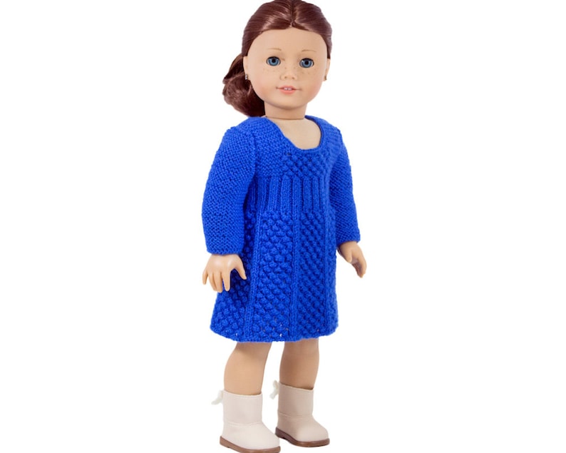 May include: A blue knitted dress for a doll. The dress has a textured pattern and a scoop neckline.