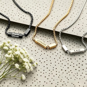 May include: Three box chain necklaces in black, gold, and silver tones. Each necklace features a rectangular bar pendant engraved with two names: Sopia and Oliver on the black bar, LEONARD and DAVID on the gold bar, and Leo and Jemas on the silver bar.