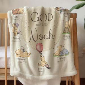 May include: A cream-colored baby blanket with a soft, plush texture. The blanket features Winnie the Pooh illustrations and the name "Noah" in elegant script. Text includes "God Says I Am" and various positive affirmations.