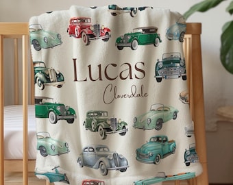 May include: A cream-colored baby blanket featuring a pattern of vintage cars in various colors, including red, green, and blue. The blanket is personalized with the name "Lucas" and the last name "Cloverdale" in brown script.