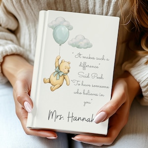 Puede incluir: Un libro personalizado con una ilustración de Winnie the Pooh. La portada presenta un globo azul claro, nubes y una cita: "It makes such a difference" y "To have someone who believes in you." El nombre "Mrs. Hannah" está impreso debajo.