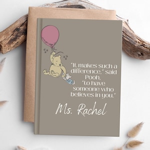 May include: A notebook with a tan cover and a grey front cover featuring a Winnie the Pooh illustration. The illustration shows Pooh holding a pink balloon with Piglet. Text reads "It makes such a difference," said Pooh, "to have someone who believes in you." Ms. Rachel.
