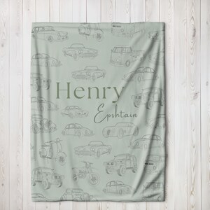 May include: A light green blanket featuring a pattern of vintage car illustrations in gray. The blanket has the name "Henry Epshtain" printed in a darker green font. The design includes various car models, motorcycles, and scooters.