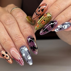 May include: Almond-shaped nails featuring a variety of Halloween-themed designs including orange glitter jack-o'-lanterns, gold pumpkins, purple backgrounds with black bats, white ghosts, and a red French tip with a white spiderweb pattern.