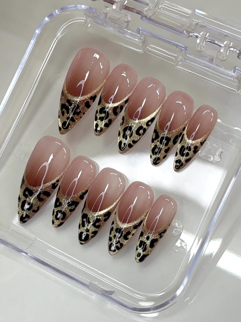 Puede incluir: Un juego de diez u&ntilde;as postizas en forma de almendra con una base de color nude y un dise&ntilde;o de punta francesa. Las puntas est&aacute;n decoradas con un fondo de purpurina dorada y un estampado de leopardo negro. Las u&ntilde;as est&aacute;n dentro de una caja transparente.
