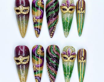 Può includere: Un set di dieci unghie finte lunghe e appuntite a tema Mardi Gras. I disegni includono glitter, maschere, gigli e motivi a vortice in viola, verde e oro. Alcune unghie presentano accenti gioiello.
