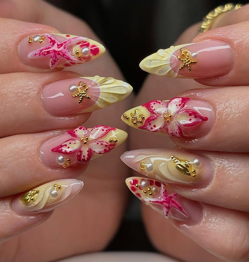 May include: A set of almond-shaped, professionally manicured nails. Each nail features a unique design with pink, yellow, and white floral and starfish accents. Gold embellishments and small pearls add detail to the nail art.