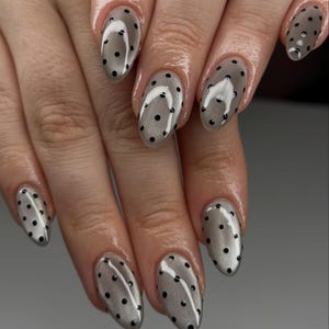 May include: A set of polished fingernails with a gray, semi-transparent base and small black polka dots. The nails are oval-shaped and have a glossy finish, creating a stylish and modern look.