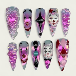May include: A collection of ten long, pointed false nails with diverse designs. The nails display iridescent hues of pink, purple, and silver, with designs like hearts, clown faces, and geometric patterns. Some nails incorporate 3D elements.
