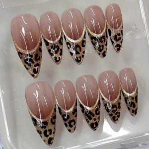 Puede incluir: Un juego de diez u&ntilde;as postizas en forma de almendra con una base de color nude. Cada u&ntilde;a presenta un dise&ntilde;o de punta francesa en forma de V profunda con un borde de purpurina dorada y un estampado de leopardo negro y marr&oacute;n en la punta.