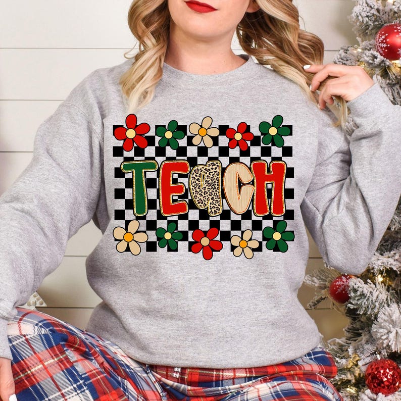 Pu&ograve; includere: Una felpa grigia con la scritta "TEACH" in un design colorato. Le lettere sono bordate di verde, rosso e beige, con una "C" con stampa leopardata. Il design include uno sfondo a scacchi e accenti floreali in rosso, verde e crema.