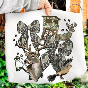 May include: White graphic featuring a deer head with a bow and arrow, a deer, a dove, a hunting blind, and camouflage bows. The design incorporates brown, green, and white elements, with deer tracks scattered throughout.
