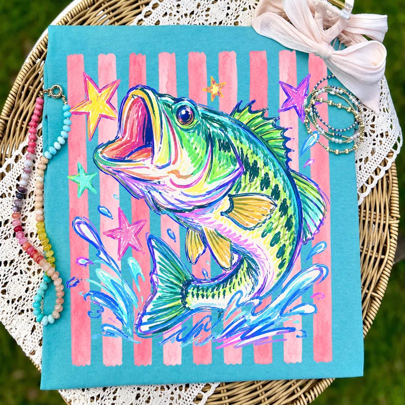 Op de afbeelding: Een turquoise draagtas met een kleurrijke illustratie van een largemouth bass met open mond, omringd door sterren en waterspetters. De achtergrond heeft roze verticale strepen. Een kralenketting en armbanden zijn zichtbaar.