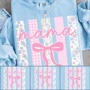Może przedstawiać: Jasnoniebieska bluza z napisem "mama" w r&oacute;żowym skrypcie, zaakcentowana r&oacute;żową kokardą oraz kwiatowymi i kratkowanymi paskami. Na dole zdjęcia znajdują się trzy dodatkowe wzory ze słowami "mimi", "nana" i "gigi".
