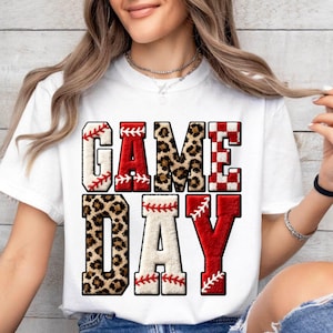 May include: White t-shirt with the words "GAME DAY" in a baseball-themed design. The letters feature baseball stitching, leopard print, and a red and white checkered pattern. A sporty and fun design.