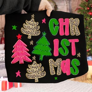 May include: Black Christmas-themed graphic with the word "CHRISTMAS" in green, pink, and leopard print. The design includes Christmas trees and stars in various colors and patterns.