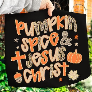 May include: Black tote bag with the words "PUMPKIN SPICE & JESUS CHRIST" in orange and leopard print lettering. The design includes a pumpkin, acorn, cross, stars, and a maple leaf.