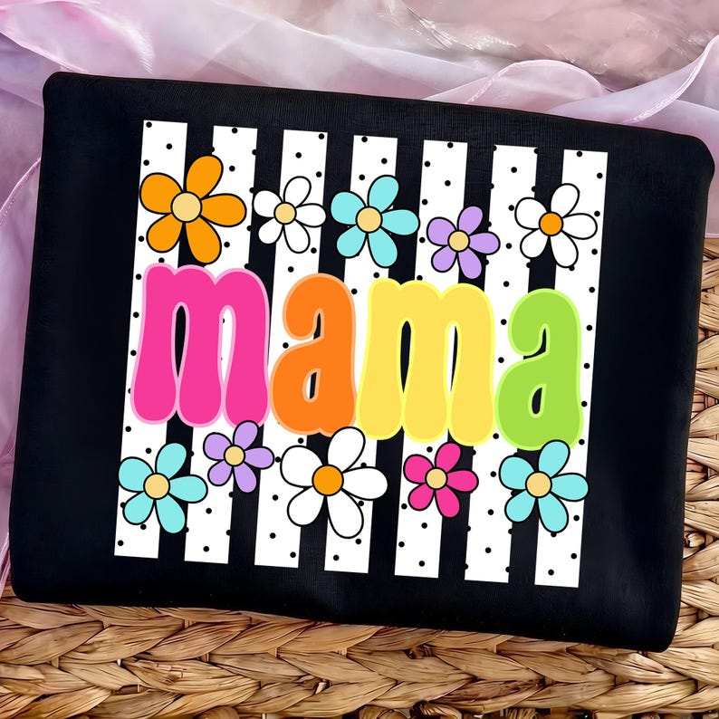 May include: Black t-shirt with a white striped design and colorful flowers. The word "mama" is displayed in large, retro-style letters in pink, orange, yellow, and green. The shirt has a playful and cheerful design.