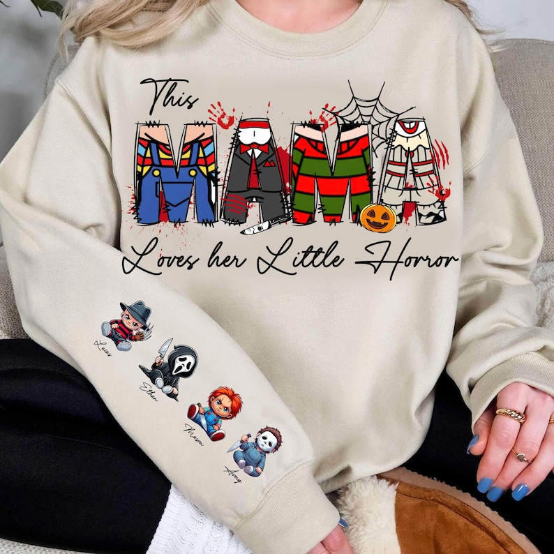Pu&ograve; includere: Una felpa beige con la scritta "This Mama Loves her Little Horror". La parola "Mama" &egrave; disegnata con personaggi di film horror. La manica presenta personaggi horror dei cartoni animati. Un capo d'abbigliamento a tema Halloween.