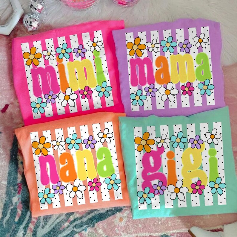 May include: Four colorful t-shirts with floral designs and names: "Mimi," "Mama," "Nana," and "Gigi." Each shirt features a different pastel color, white stripes, and a variety of flower illustrations. The names are in bold, bubble letters.