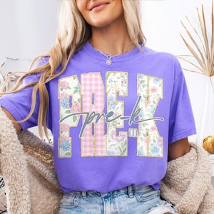 May include: A lilac t-shirt featuring the text "PRE-K" in a floral and gingham design, with gold outlines. The shirt is a solid lilac colour.