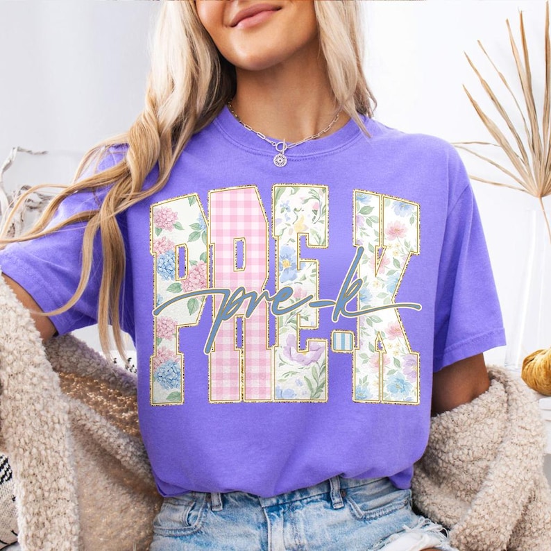 May include: A lilac t-shirt featuring the text "PRE-K" in a floral and gingham design, with gold outlines. The shirt is a solid lilac colour.