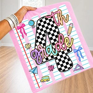 May include: A pink blanket featuring a large black and white checkered number 4 with the text 4th grade in neon-colored script. The design includes school-themed graphics like a globe, pencil, paper airplane, school bus, and bows on lined paper.