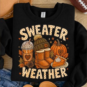 May include: A black crewneck sweatshirt featuring a graphic print with the text "SWEATER WEATHER" in a tan polka-dot font. The design includes a coffee cup, a knit beanie, a pair of tan boots, a pumpkin, and a slice of pumpkin pie with whipped cream.