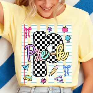 May include: A pale yellow t-shirt featuring a graphic print of a large letter P with a black and white checkerboard pattern. The design includes the text Pre-k in colorful script, surrounded by school-themed icons like a bus, pencil, and globe.