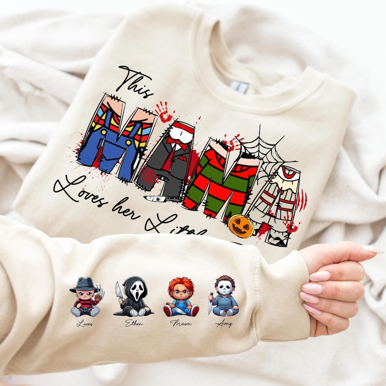 Pu&ograve; includere: Felpa color crema con la scritta "This Mama Loves her Littles" in corsivo nero. La parola "Mama" &egrave; disegnata con personaggi di film horror. La manica presenta quattro piccole illustrazioni di personaggi con nomi.