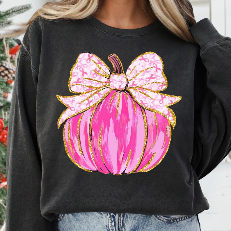 May include: Black sweatshirt featuring a pink pumpkin design with a gold glitter outline. The pumpkin has a large bow with pink ribbon accents. The design is centered on the front of the shirt.