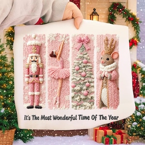 May include: A pink and white Christmas-themed artwork featuring a nutcracker, ballerina, Christmas tree, and mouse king. The artwork is embroidered with the text "It's The Most Wonderful Time Of The Year". The artwork is held by a person.