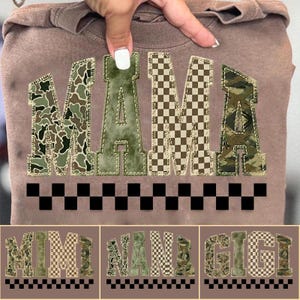 Op de afbeelding: Een bruine sweatshirt met het woord "MAMA" in grote patchwork letters. De letters hebben een camouflage- en dambordpatroon. Onder het woord "MAMA" bevindt zich een zwart-wit dambordrand. Daaronder staan drie kleinere sweatshirts met de woorden "MIMI", "NANA" en "GIGI".