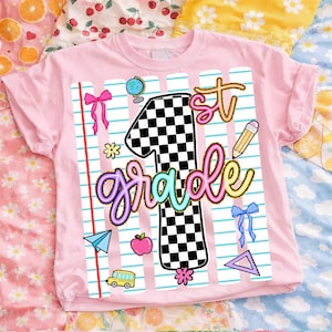 May include: A light pink t-shirt featuring a graphic design of a large number one with a black and white checkerboard pattern. The text 1st grade is written in colorful script. The design includes school-themed icons like a globe, pencil, apple, paper airplane, and bows on a background of blue lined notebook paper.