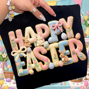 以下が含まれることがあります： 「HAPPY EASTER」の文字が3Dデザインで施された黒いTシャツ。文字はパステルピンク、ブルー、イエローで、ウサギ、卵、花で装飾されています。デザインは、織り込まれたような質感です。