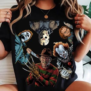 May include: Black t-shirt with a graphic design of horror movie characters, including Michael Myers, Jason Voorhees, Freddy Krueger, Chucky, and Pennywise. The characters are shown with their iconic weapons and masks.