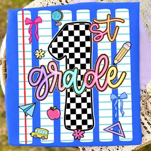 May include: A blue t-shirt featuring a graphic print of a large black and white checkered number one, the text 1st grade in colorful script, and school-themed icons including a globe, pencil, apple, school bus, paper plane, and bows.