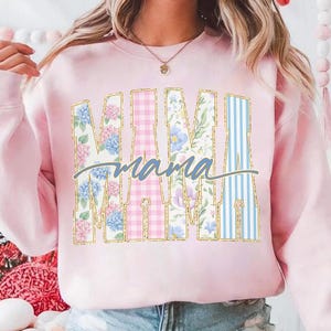 May include: Pink sweatshirt with the word "MAMA" in large, decorative letters. The letters are filled with floral, gingham, and striped patterns. The word "mama" is written in cursive below the letters.