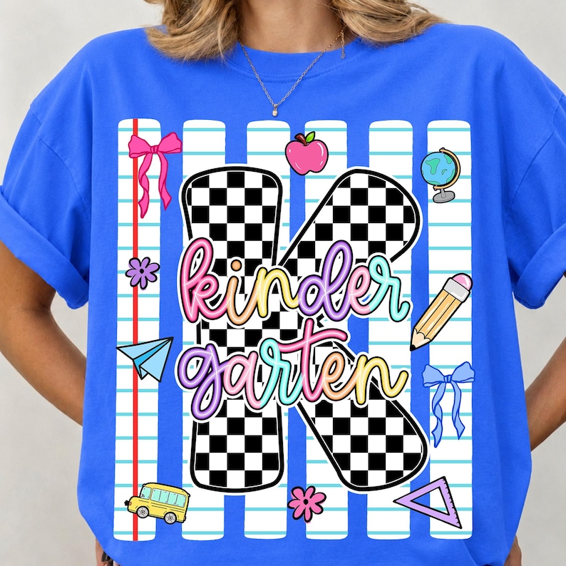 May include: A bright blue t-shirt featuring a large black and white checkered letter K with the word kindergarten written in a colorful gradient script. The design includes school-themed icons like a pencil, apple, globe, bus, and bows.