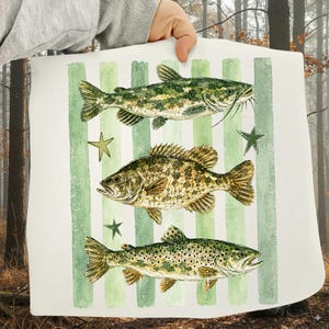 May include: A white rectangular decorative pillow featuring three detailed illustrations of fish in shades of green and brown. The fish are set against a background of vertical green stripes and accented with green star shapes.