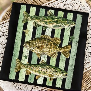 May include: Black square fabric with a design featuring three detailed fish illustrations in shades of green and brown, set against a backdrop of black and green vertical stripes. The design includes green star accents.