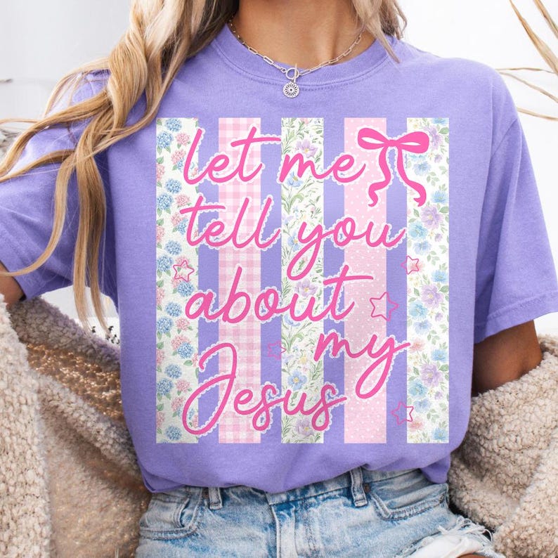 K&ouml;nnte beinhalten: Ein lilafarbenes T-Shirt mit dem rosa Schriftzug "Let me tell you about my Jesus". Der Text ist vor vertikalen Streifen mit Blumen- und Vichy-Mustern platziert.