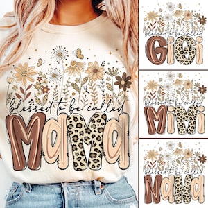 May include: Cream-colored sweatshirt featuring the text "blessed to be called MAMA" in brown and leopard print. The design includes floral and butterfly graphics. Additional designs say "Gigi", "Mimi", and "Nana".