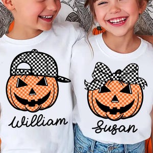 May include: Two children wearing white t-shirts with Halloween-themed pumpkin designs. One shirt features a pumpkin wearing a checkered hat, the other a checkered bow. The names "William" and "Susan" are written below the pumpkins.
