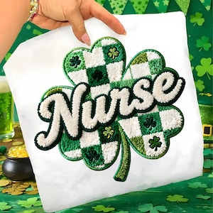 May include: White t-shirt featuring a large, embroidered shamrock design in shades of green and white. The word "Nurse" is embroidered in white, with a green outline. The shamrock has a checkered pattern and small shamrock accents.