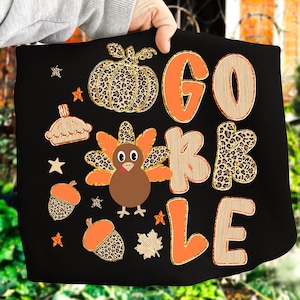 Può includere: Grafica nera a tema Thanksgiving con le parole "GOBBLE" in arancione e trame effetto legno. Include una zucca, un tacchino, una torta, ghiande, stelle e una foglia d'acero.